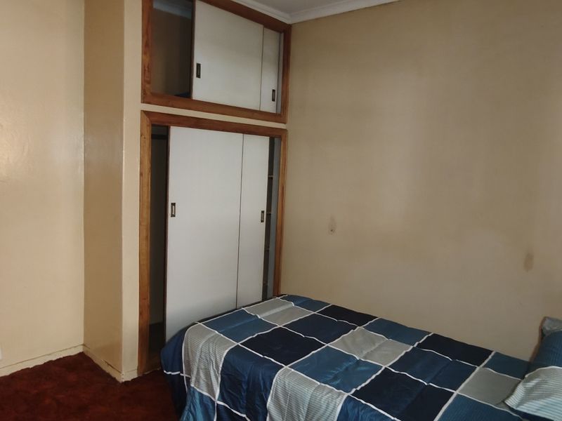 A bedroom featuring built-in wardrobes with overhead storage and carpeted flooring, requiring cosmetic updates to the wall finishes.