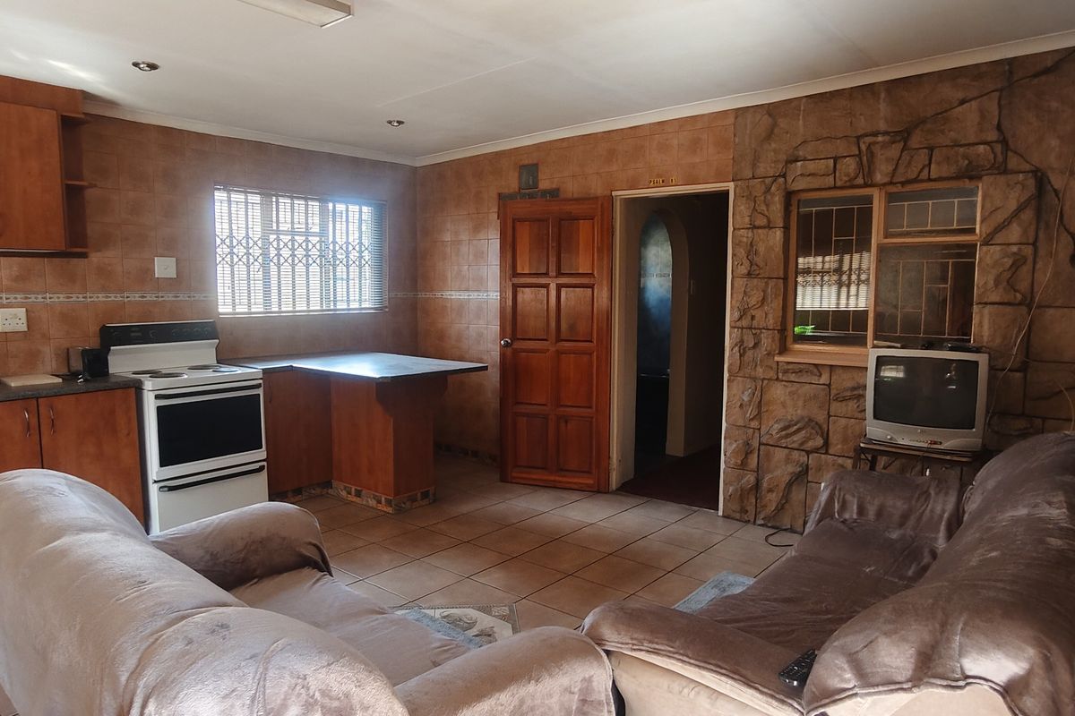 Open-plan living and kitchen area featuring wooden cabinetry, tiled surfaces, and a stone-cladding feature wall, offering a dated but functional layout.