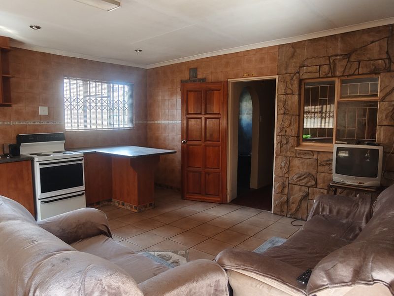 Open-plan living and kitchen area featuring wooden cabinetry, tiled surfaces, and a stone-cladding feature wall, offering a dated but functional layout.