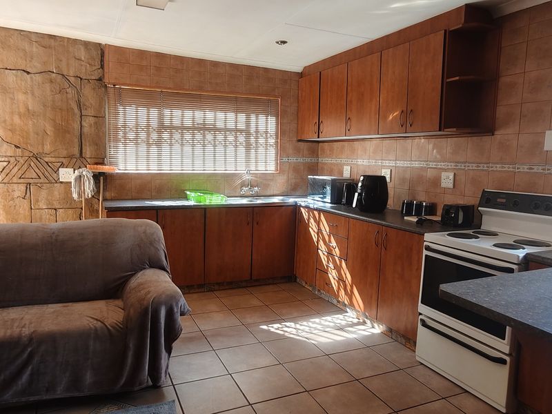 Open plan kitchen and living area featuring wooden cabinetry, tiled flooring, and a distinctive stone feature wall, offering a functional layout for daily living.