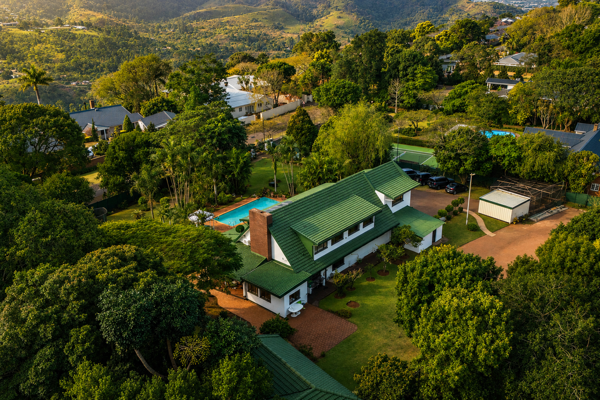 Aerial view of a residential property featuring a green tiled roof, swimming pool, landscaped garden, and paved driveway set within a lush green environment.