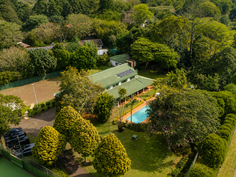 Aerial view of a spacious property featuring a large landscaped garden, swimming pool, tennis court, and a main residence equipped with solar panels.
