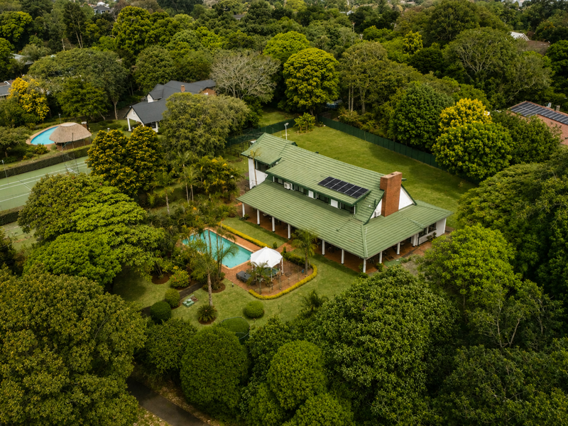 Aerial view of a large residential property featuring a swimming pool, tennis court, lush garden, and a house with solar panels and a tiled roof.