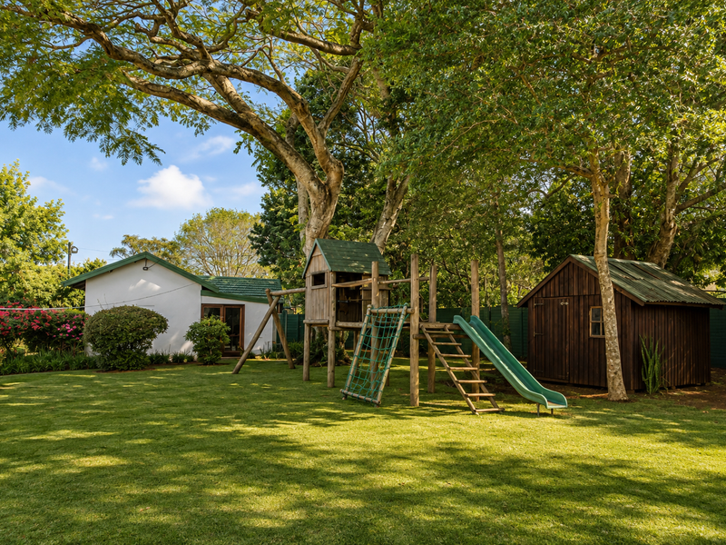 A spacious, well-maintained garden featuring a lush lawn, mature trees, a wooden shed, and a separate outbuilding, providing a serene outdoor environment.