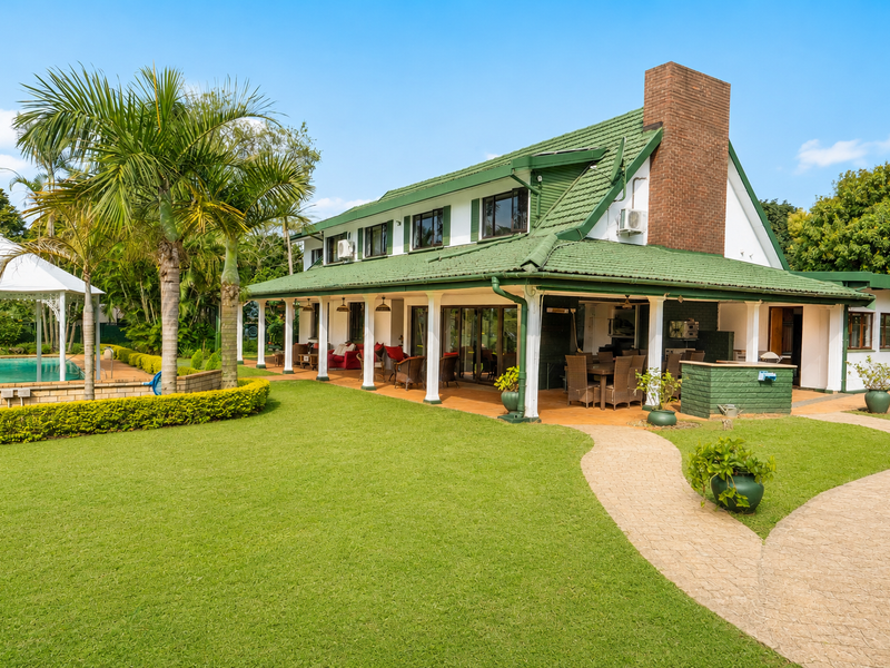 Spacious rear exterior featuring a large covered patio, built-in braai area, swimming pool with gazebo, and a well-maintained landscaped garden.