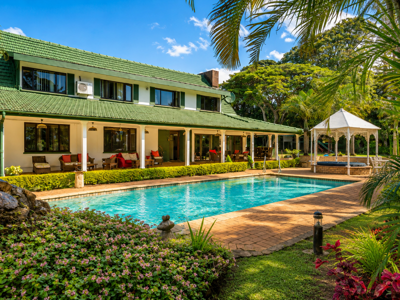 A spacious rear garden featuring a large swimming pool, brick-paved deck, covered patio, and a charming gazebo with an integrated jacuzzi.