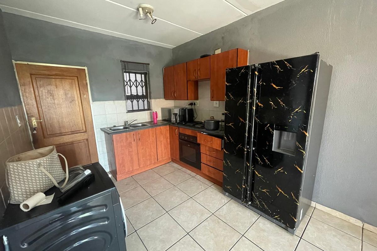 A functional kitchen featuring built-in wooden cabinetry, a double sink, and a built-in oven, with tiled flooring and a window security gate.