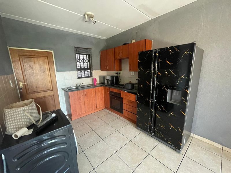 A functional kitchen featuring built-in wooden cabinetry, a double sink, and a built-in oven, with tiled flooring and a window security gate.