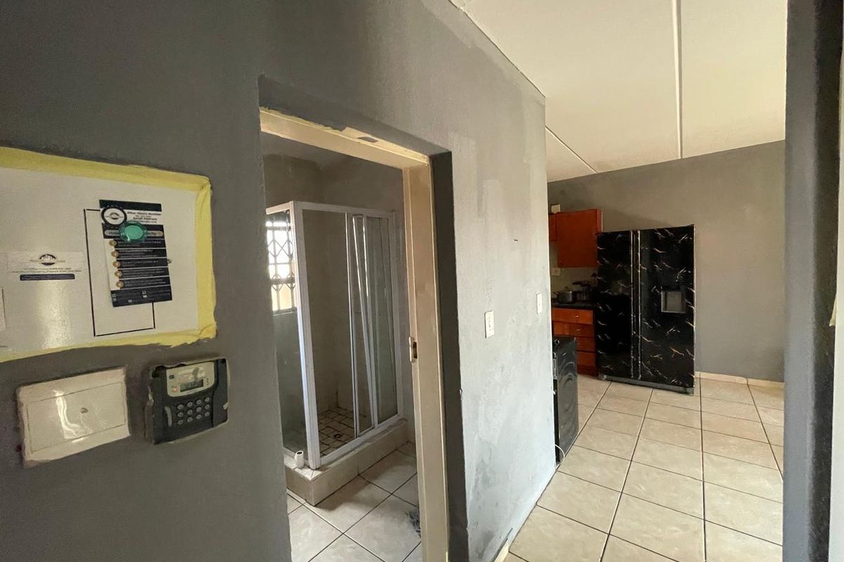 Open plan living area featuring tiled flooring and a connected bathroom with a shower enclosure, requiring cosmetic updates and finishing touches.