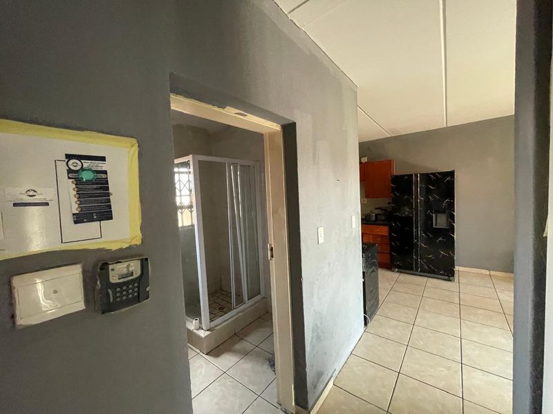 Open plan living area featuring tiled flooring and a connected bathroom with a shower enclosure, requiring cosmetic updates and finishing touches.