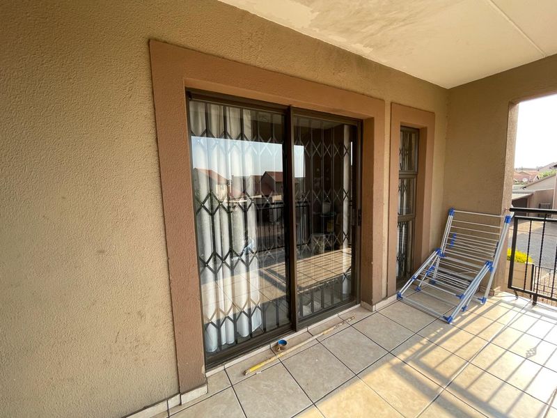 A covered balcony featuring tiled flooring, a sliding glass door with security gate, and metal railings, showing minor ceiling water staining.