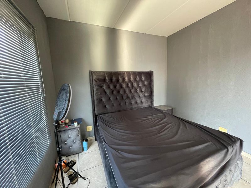 A bedroom featuring grey painted walls, tiled flooring, and venetian blinds, providing a neutral foundation for personal styling.