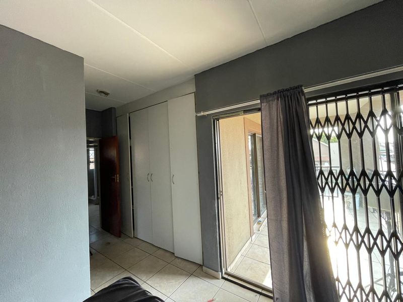 A bedroom featuring built-in cupboards, tiled flooring, and a sliding glass door leading to a balcony with a security gate.