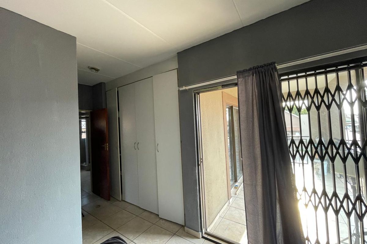 A bedroom featuring built-in cupboards, tiled flooring, and a sliding glass door leading to a balcony with a security gate.