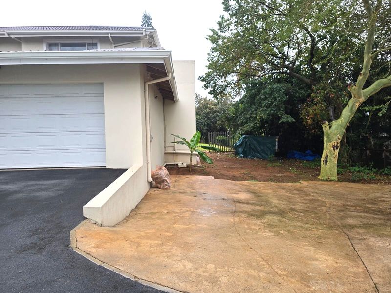 Front exterior view of the property featuring a garage, concrete driveway, and adjacent garden area with mature trees.