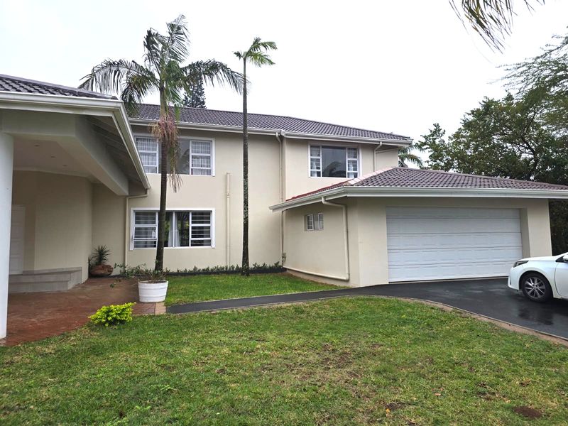 Front elevation of a double-story residential house featuring a tiled roof, double garage, paved driveway, and a covered entrance area.