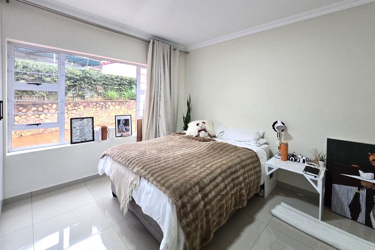 A well-lit bedroom featuring large aluminium windows, neutral tiled flooring, and classic cornice detailing, offering a bright and comfortable living space.