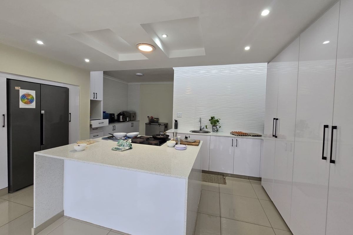 Modern kitchen featuring a large central island with quartz countertops, sleek white cabinetry, recessed lighting, and a textured feature wall.