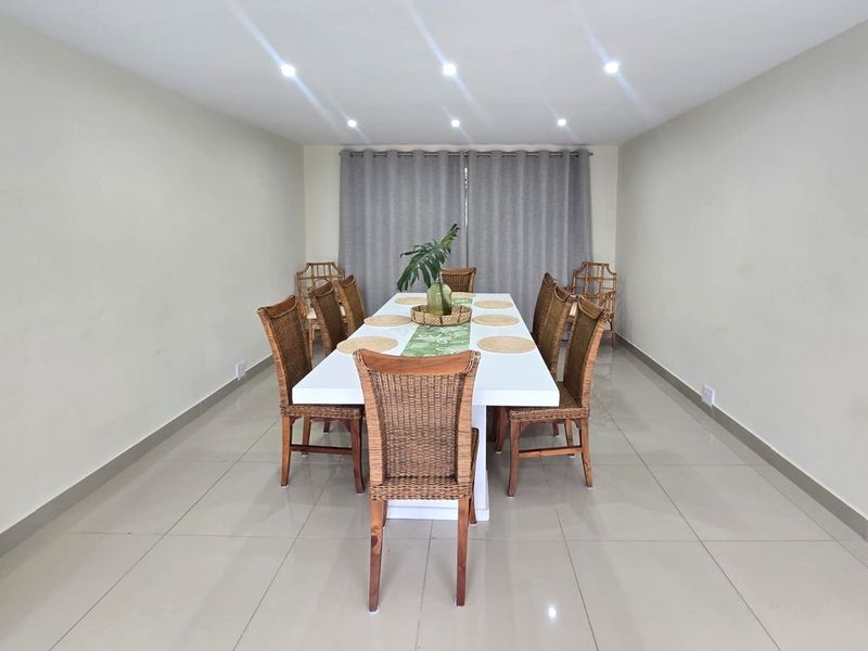 A bright and spacious dining room featuring neutral walls, large format porcelain floor tiles, and recessed ceiling downlights.