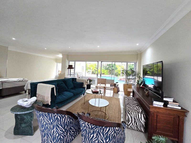 Spacious open-plan living area featuring tiled floors, recessed lighting, and large sliding glass doors providing direct access to the outdoor pool area.