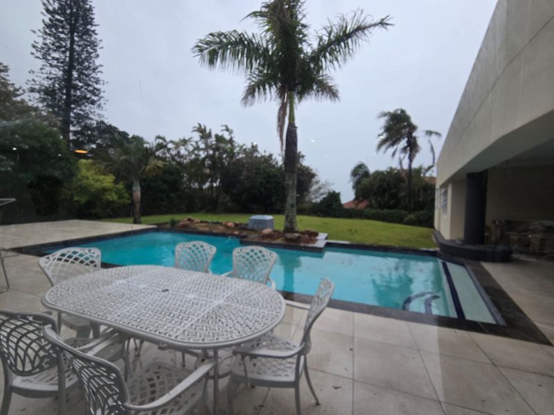 Outdoor patio area featuring a swimming pool, tiled flooring, and a landscaped garden with mature palm trees.