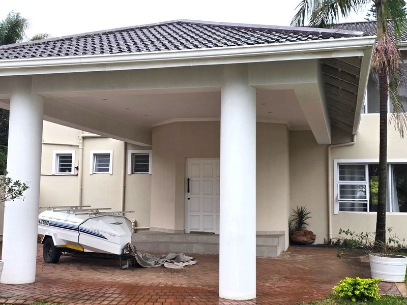 Front elevation of the house featuring a covered entrance with prominent concrete columns, tiled roof, and paved driveway area.