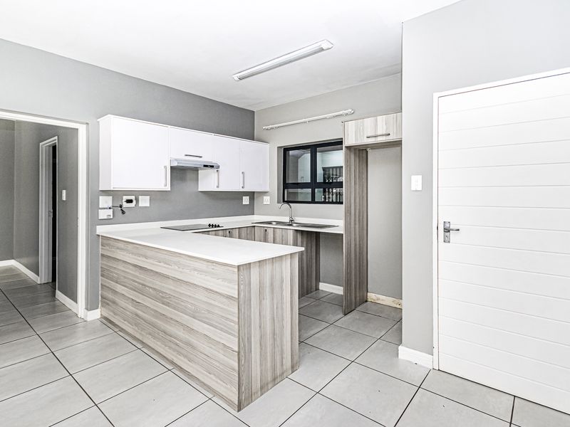 Modern kitchen featuring light wood-grain cabinetry, white countertops, integrated hob with extractor, and neutral tiled flooring in an open-plan layout.