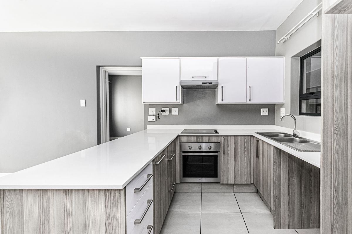 Modern kitchen featuring light wood-grain cabinetry, white quartz countertops, built-in oven, electric hob, extractor fan, and a stainless steel double sink.