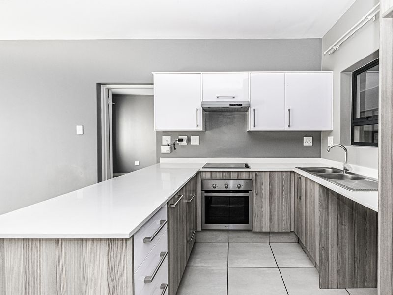 Modern kitchen featuring light wood-grain cabinetry, white quartz countertops, built-in oven, electric hob, extractor fan, and a stainless steel double sink.