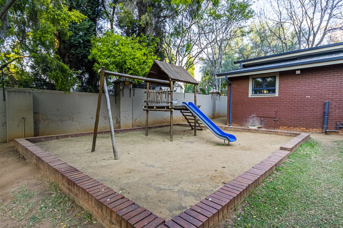 Rear garden area featuring a sand pit with brick edging, a brick facade building, and a boundary wall with visible plaster wear.