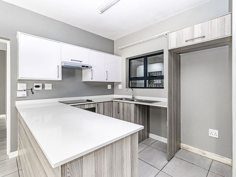 Modern kitchen featuring white and wood-grain cabinetry, stone countertops, integrated hob, extractor fan, and tiled flooring in a clean, open-plan layout.
