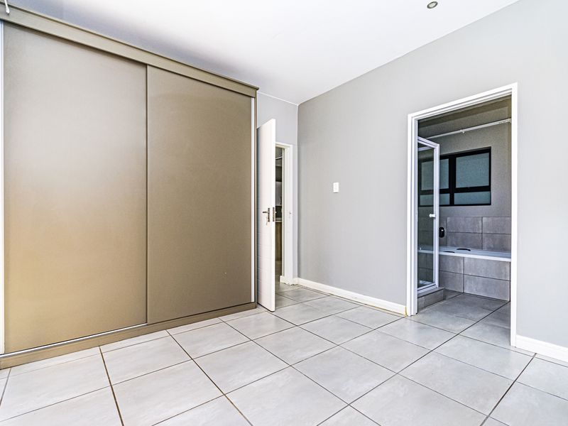 A bright, empty bedroom featuring neutral tiled flooring, a large built-in sliding wardrobe, and direct access to an en-suite bathroom.
