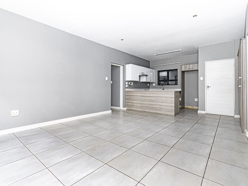 An open-plan living and kitchen area featuring neutral grey walls, tiled flooring, and modern kitchen cabinetry with a breakfast bar island.
