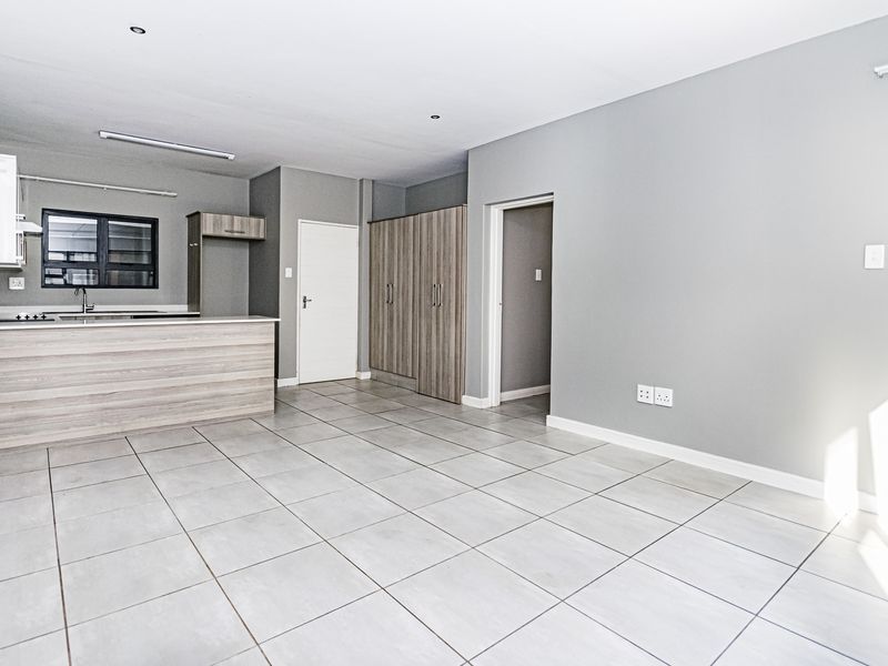 An open-plan living and kitchen area featuring modern tiled flooring, built-in cabinetry, and integrated kitchen appliances in a clean, neutral space.