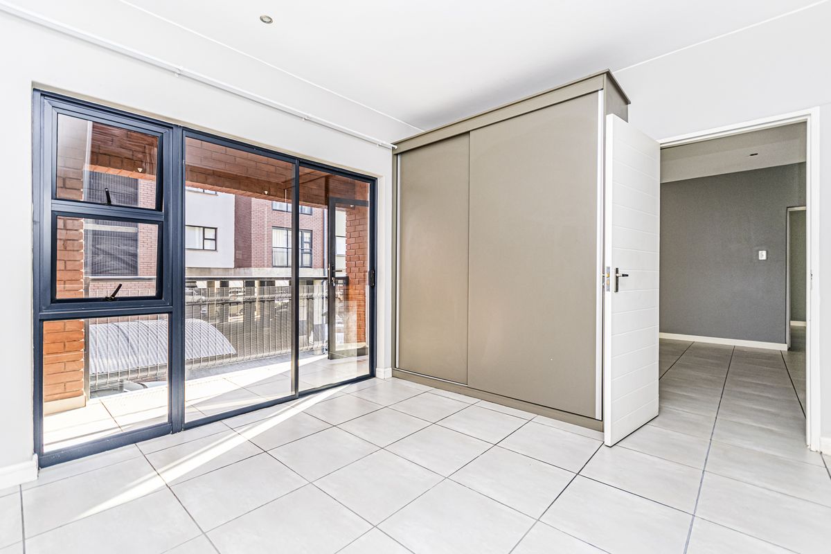 A bright, empty bedroom featuring tiled flooring, a built-in sliding door wardrobe, and large aluminium sliding doors leading to a balcony.