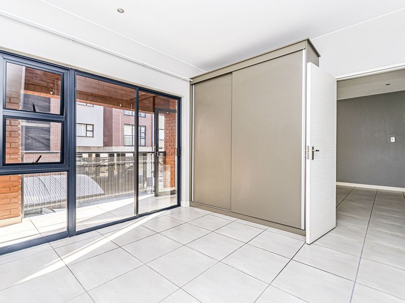 A bright, empty bedroom featuring tiled flooring, a built-in sliding door wardrobe, and large aluminium sliding doors leading to a balcony.