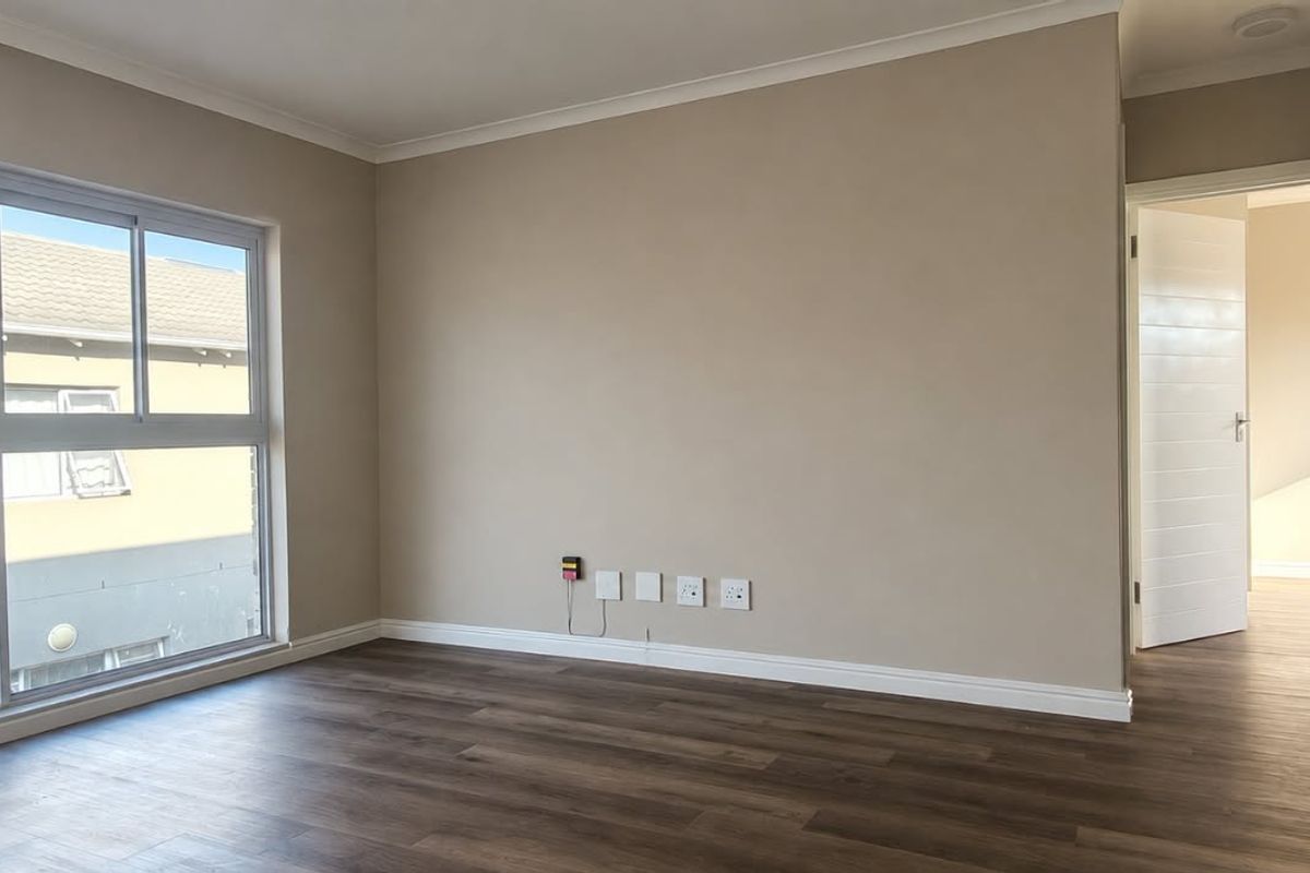 A bright and spacious living area featuring modern laminate flooring, neutral wall tones, and large sliding windows providing natural light.