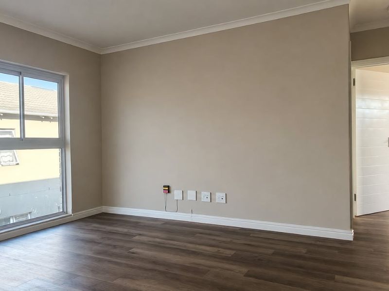 A bright and spacious living area featuring modern laminate flooring, neutral wall tones, and large sliding windows providing natural light.