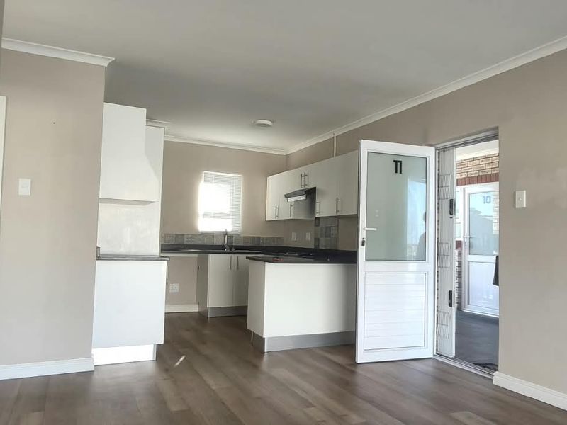 Open-plan living area featuring laminate flooring and a functional kitchen with built-in cabinetry, extractor fan, and direct access to an outdoor space.