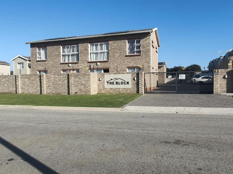 Front exterior view of a brick apartment complex featuring a secure gated entrance, paved driveway, and perimeter wall with electric fencing.