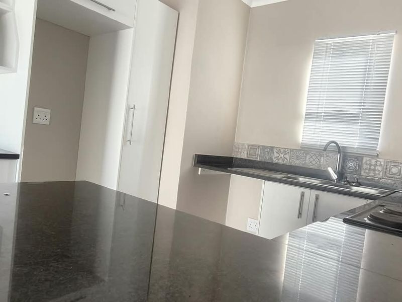 A modern, clean kitchen featuring dark granite countertops, patterned tile backsplash, built-in cabinetry, and an integrated electric hob.