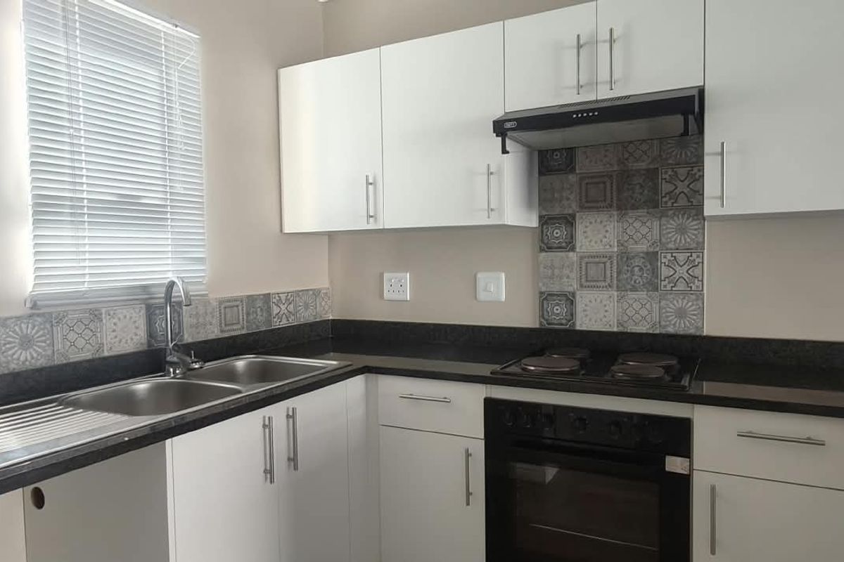 Modern kitchen featuring white cabinetry, dark granite countertops, patterned tile backsplash, and integrated stainless steel appliances.