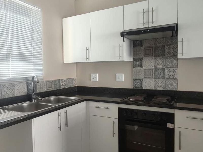 Modern kitchen featuring white cabinetry, dark granite countertops, patterned tile backsplash, and integrated stainless steel appliances.