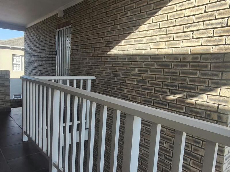 A covered balcony featuring brick walls, tiled flooring, and a white railing, providing an outdoor space for the apartment.