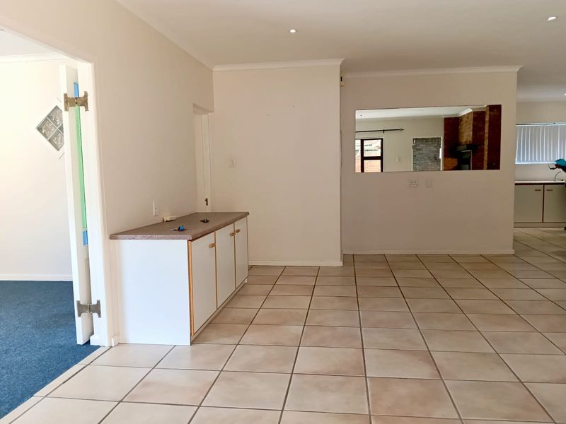 Spacious open-plan living area featuring neutral tiled flooring, built-in cabinetry, and an internal window looking through to the adjacent room.