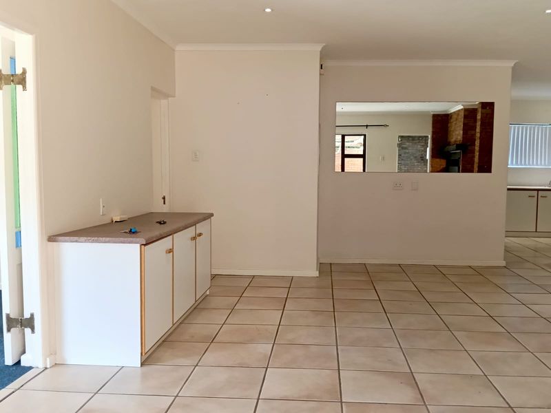 Spacious open-plan living area featuring neutral ceramic floor tiles, built-in cabinetry with a laminate countertop, and a large internal wall cutout for natural light.