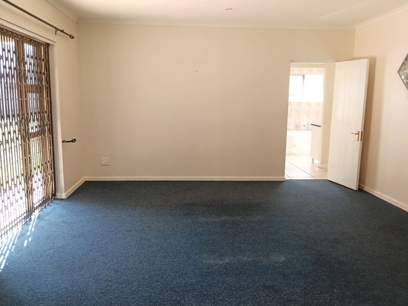An empty living room featuring blue carpeting, a security gate leading to the exterior, and access to an adjacent bathroom.