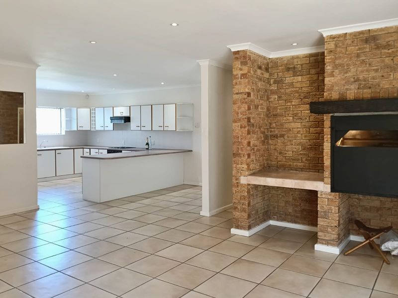 Spacious open-plan living area featuring a prominent brick fireplace and a functional kitchen with ample cabinetry and tiled flooring throughout.