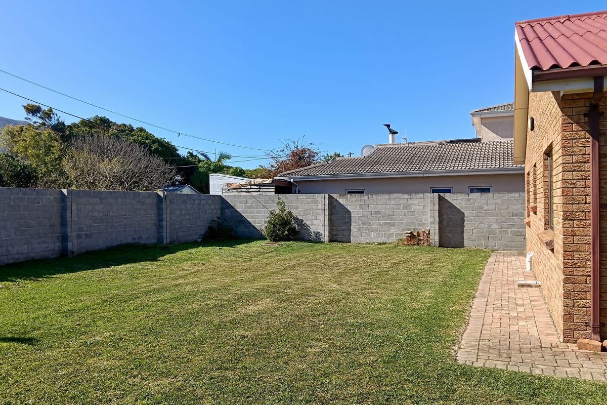 A private rear garden featuring a lawn, paved walkway, and secure brick boundary walls adjacent to the house exterior.