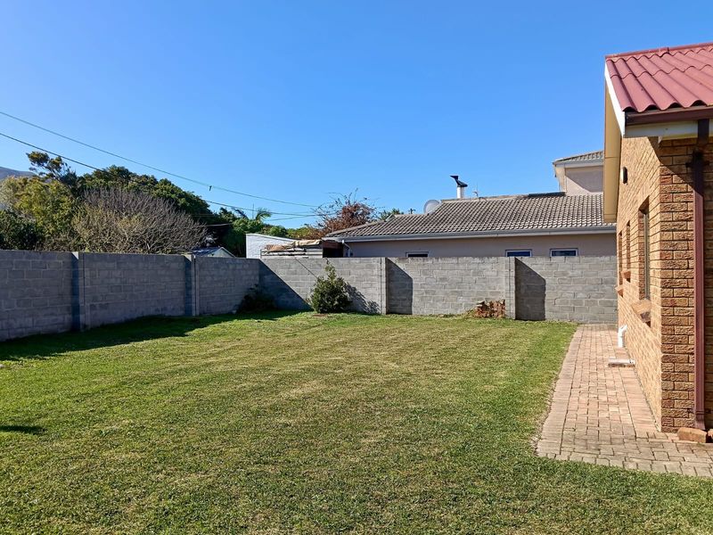 A private rear garden featuring a lawn, paved walkway, and secure brick boundary walls adjacent to the house exterior.